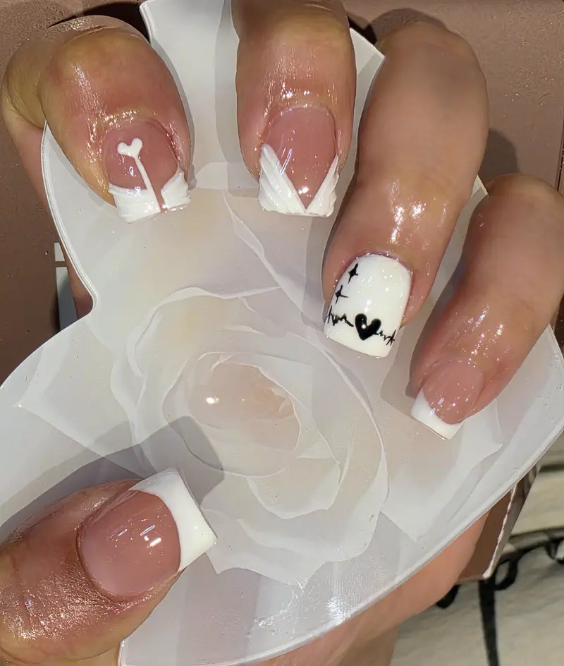 Short nude nails with white French tips and small heart details